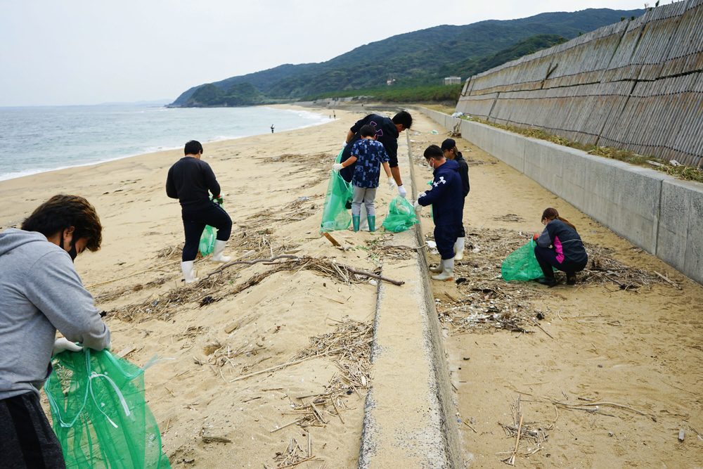 砂浜で網袋を持ち、漂着ゴミを拾う参加者たち