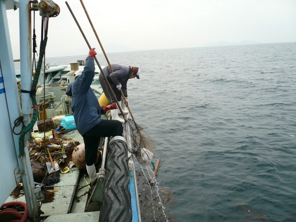 漁船の上から竿で海のゴミを引き上げる漁師
