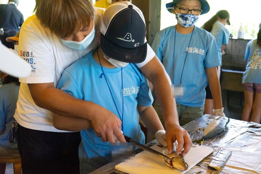 魚のさばき方を子どもに手を添えて教えるメンバー